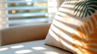Decorative pillow with tropical palm leaf shadow pattern in morning sunlight through window blinds creating geometric stripes effect on soft fabric surface.