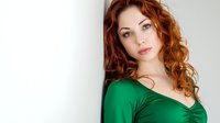 Young Caucasian woman with curly red hair wearing green top against white background for portrait photography and commercial use.