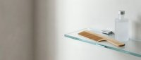 Wooden soap dish with bar soap on glass shelf next to white bottle in minimalist bathroom setting for home decor and wellness design projects.