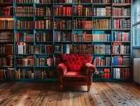 Luxurious red leather armchair against floor-to-ceiling bookshelf with vintage books in library interior, wooden floor and natural window light.