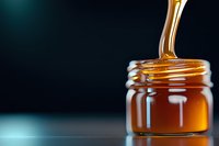 Golden honey dripping in slow motion into glass jar against dark background, capturing viscous liquid flow with amber translucent glow and smooth texture.
