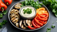 Fresh hummus dip served with grilled mushrooms, colorful bell peppers, and herbs on dark plate against gray background, healthy Mediterranean appetizer platter.