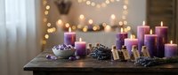 Purple candles of various sizes arranged on rustic wooden table with pinecones and warm bokeh lights creating cozy holiday atmosphere for home decor.