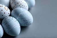 Delicate light blue Easter eggs decorated with white and gold dot patterns arranged on dark background, creating elegant holiday composition for seasonal decor.