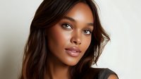 Young African American woman with natural makeup and long dark hair wearing black top poses against light background, expressing confidence and grace.