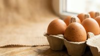 Fresh brown eggs in cardboard carton on rustic wooden table with warm natural lighting for cooking and baking recipes.