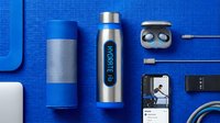 Flat lay arrangement of modern tech gadgets and accessories including wireless earbuds, portable speaker, smartwatch, charging cables, and smartphone on vibrant blue textured background for lifestyle and technology content.