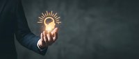 Businessman hand holding glowing lightbulb with radiating lines representing innovation, creativity, and bright ideas for business solutions and inspiration.