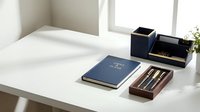 Modern minimalist office desk setup with navy blue notebook, wooden pen holder, and black desk organizer in bright natural light workspace.