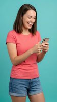 Happy young woman texting on smartphone wearing coral t-shirt and denim shorts against turquoise background for social media and communication concepts.