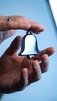 Male hands holding a shiny silver bell on a soft blue background, symbolizing alerts, notifications, and holiday celebration concepts.