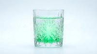 Refreshing green beverage in crystal cut glass with ice cubes on white background, suitable for beverage, drink, and hospitality design projects.