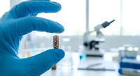 Laboratory scientist in blue gloves examining test tube sample with microscope in background for medical research and scientific analysis.