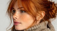 Young redhead woman with freckles and messy bun hairstyle wearing cozy knit sweater, natural beauty portrait for lifestyle and fashion content.