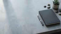 Minimalist workspace with black notebook, pen and succulent plant on concrete desk surface for productivity and organization.