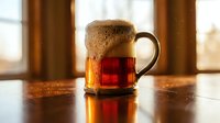Rustic ceramic mug filled with amber tea on wooden table by window with warm natural lighting creating cozy atmosphere for relaxation and comfort.