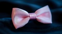 Pink grosgrain ribbon bow tie on dark blue fabric background, elegant accessory for formal events and celebrations. Close up macro photography with soft focus.