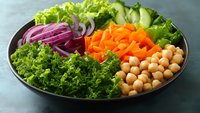 Fresh colorful salad bowl with kale, chickpeas, carrots, red onion and cucumber on dark plate. Healthy vegetarian meal for clean eating and nutrition.