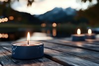 Peaceful candles glowing on wooden deck overlooking serene mountain lake at twilight creating warm ambient atmosphere for relaxation and meditation.