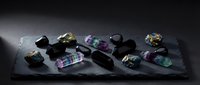 Collection of raw fluorite crystals and polished gemstones arranged on dark slate surface showcasing natural mineral specimens for geology education.