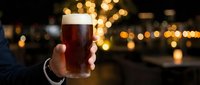 Hand holding a cold dark beer glass with golden bokeh lights in the evening background, perfect for beverage, pub, and lifestyle marketing.