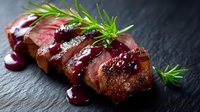 Juicy sliced duck breast with cherry sauce and fresh rosemary served on dark slate background, medium rare meat preparation for restaurant menu.
