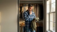 Middle-aged Caucasian man in blue shirt standing in organized walk-in closet choosing outfit, morning routine lifestyle concept for home organization.