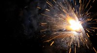 Bright welding sparks flying from metal work creating dramatic orange light burst against dark industrial background for manufacturing projects.