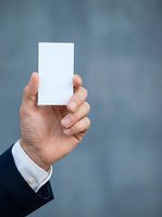 Male hand in business suit holding blank white card against blurred gray background. Suitable for corporate branding, business cards, marketing materials, and professional presentations.