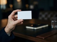 Man holding blank white business card in office environment with blurred background, suitable for corporate branding and professional networking presentations.