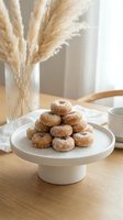 Stack of sugar-coated donuts on white ceramic cake stand with coffee cup and pampas grass in modern kitchen setting for bakery and cafe concepts.