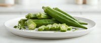 Fresh green okra pods sliced and whole on white plate, healthy vegetable ingredient for cooking and nutrition in modern kitchen setting.