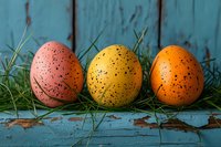 Colorful speckled Easter eggs in pink, yellow and orange arranged on rustic turquoise wooden background with fresh green grass, spring holiday celebration concept.