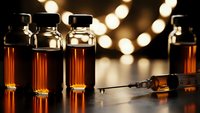 Medical vials with amber liquid and syringe on dark surface with warm bokeh lights background for healthcare and pharmaceutical concepts.