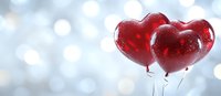 Red heart-shaped balloons floating against soft bokeh background with dreamy silver sparkles, romantic holiday celebration atmosphere for Valentine's Day or anniversary events.