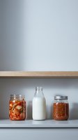 Glass jars with fermented vegetables and milk bottle on kitchen shelf for healthy probiotic food storage and meal prep organization.