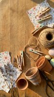 Craft supplies arranged on wooden table with floral patterned paper, twine, clothespins, terracotta pots and dried branches for creative DIY projects.