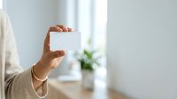 Woman holding blank white business card in hand with blurred office background, suitable for branding, corporate identity, and professional marketing materials.