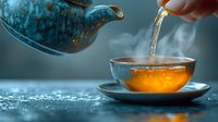Hot aromatic tea pouring from ceramic teapot into transparent cup with steam rising, captured in atmospheric blue tones with golden liquid glowing.