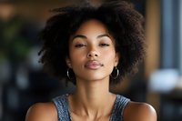 Young African American woman with natural curly hair wearing hoop earrings and denim top in modern office setting for professional business content.