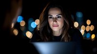 Young professional woman working late at night on laptop computer with bokeh city lights background for business and technology concepts.