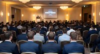 Business conference presentation with diverse professional audience in elegant hotel ballroom setting with warm lighting and projection screen.