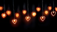 Glowing heart-shaped lights hanging on strings create romantic atmosphere against dark background for Valentine's Day celebrations and love-themed decorations.