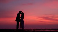 Romantic couple silhouette embracing at sunset beach with dramatic pink purple sky. Love, romance, relationship concept for wedding invitations.