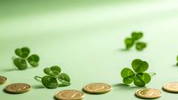 Fresh green four-leaf clovers and golden coins scattered on soft green background for St. Patrick's Day celebration and Irish luck symbols.