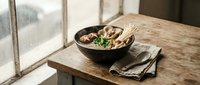 Rustic wooden bowl filled with fresh mixed salad sits on weathered farm table near bright window creating warm natural lighting for healthy eating concept.