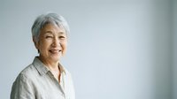 Senior Asian woman with short white hair smiling at camera against neutral background, suitable for healthcare, wellness, lifestyle and corporate portraits.