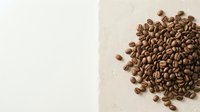 Roasted coffee beans scattered on neutral beige and white background, isolated for beverage, food, and cafe design projects.