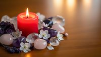 Red candle burning among healing crystals, amethyst, rose quartz and white flowers on wooden surface for meditation, spa wellness and spiritual energy cleansing.