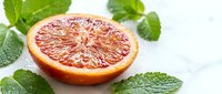Fresh grapefruit half with vibrant pink flesh and mint leaves on white background, ideal for food and beverage marketing.